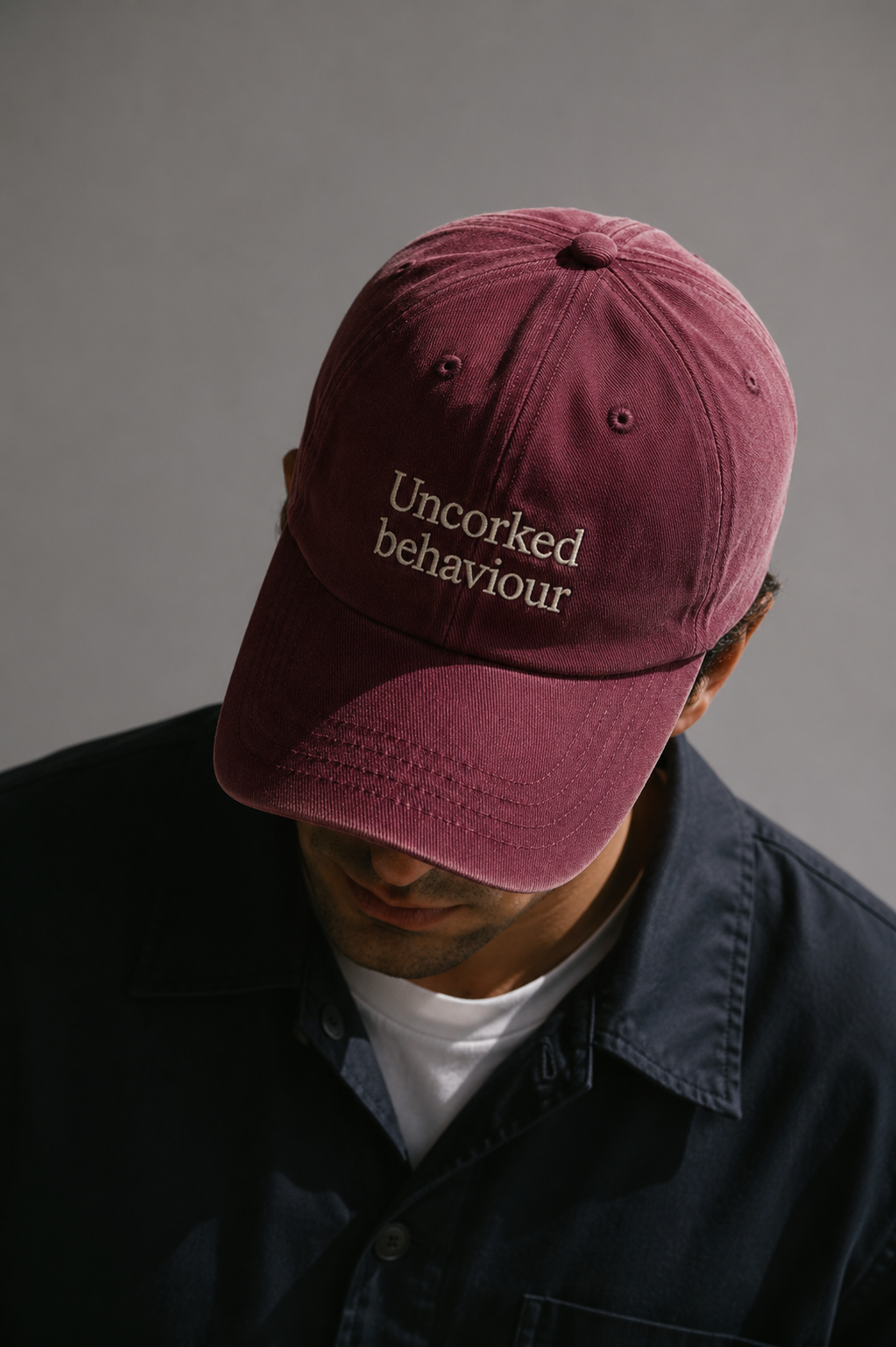 Person wearing a maroon burgandy cap with 'Uncorked behaviour' embroidered text against a brown background