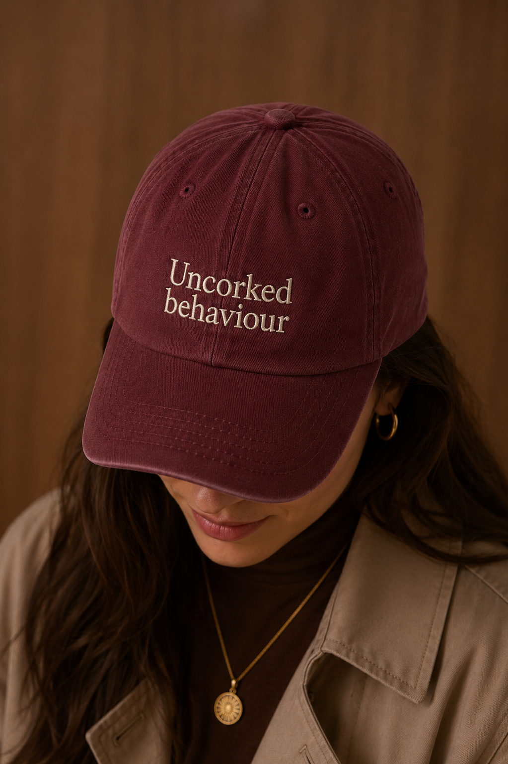 Person wearing a maroon burgandy cap with 'Uncorked behaviour' embroidered text against a brown background