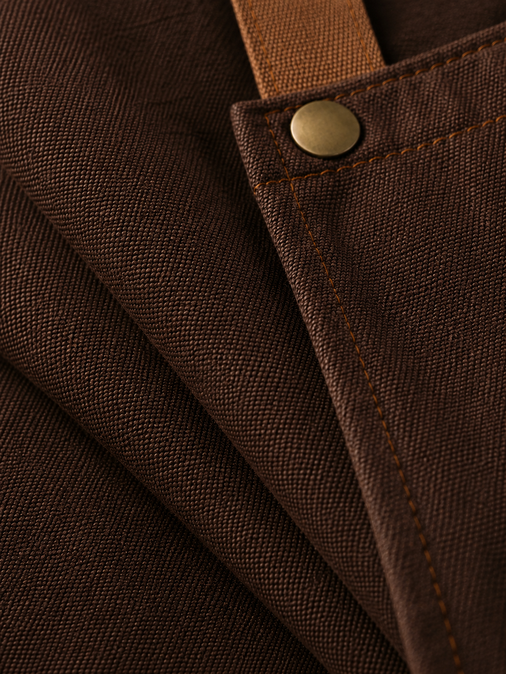 Close-up of brown fabric of apron with a button and stitching detail