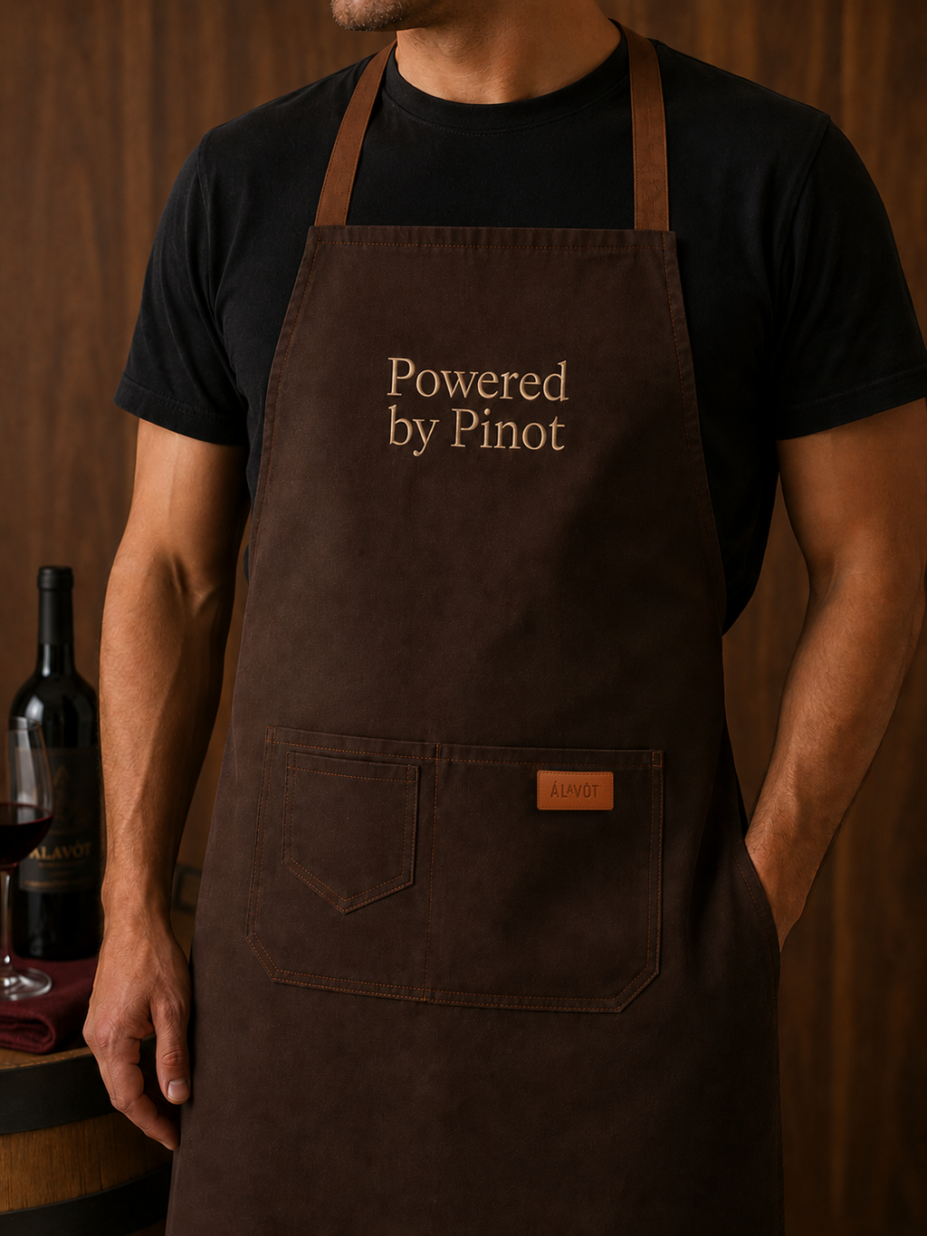 Person wearing a brown apron with 'Powered by Pinot' text, standing in a wine-themed setting. Alavot branding
