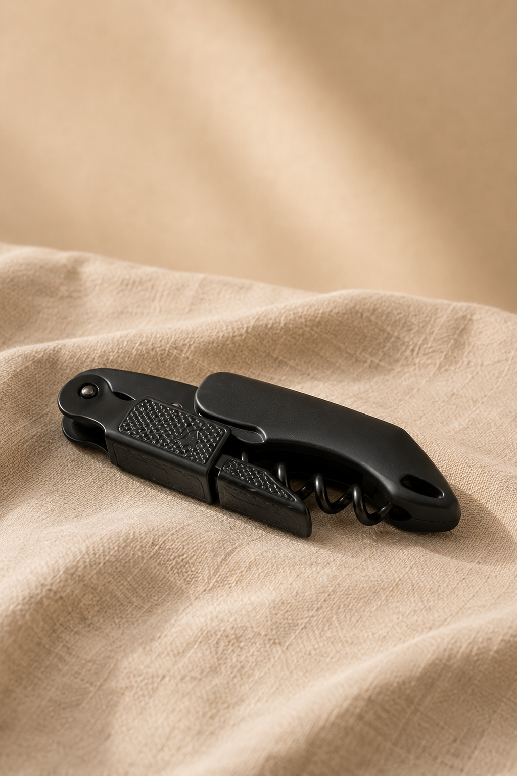 Black multi-too bottle opener on a beige fabric background