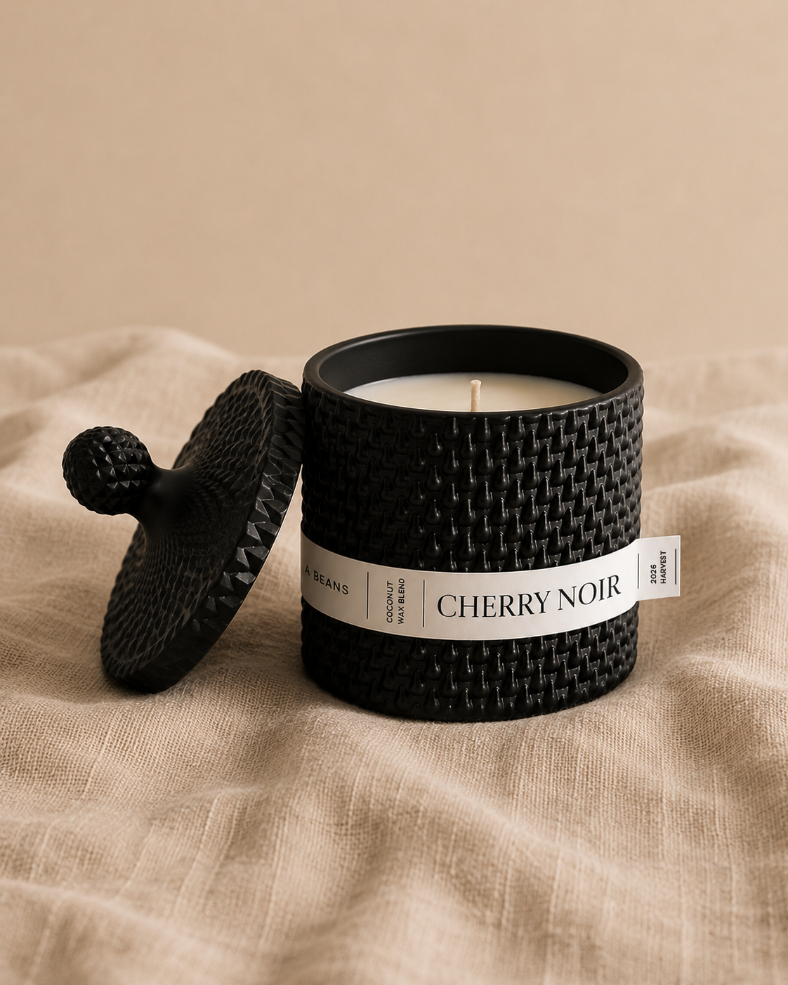 Black scented candle with 'Cherry Noir' label on a beige fabric background