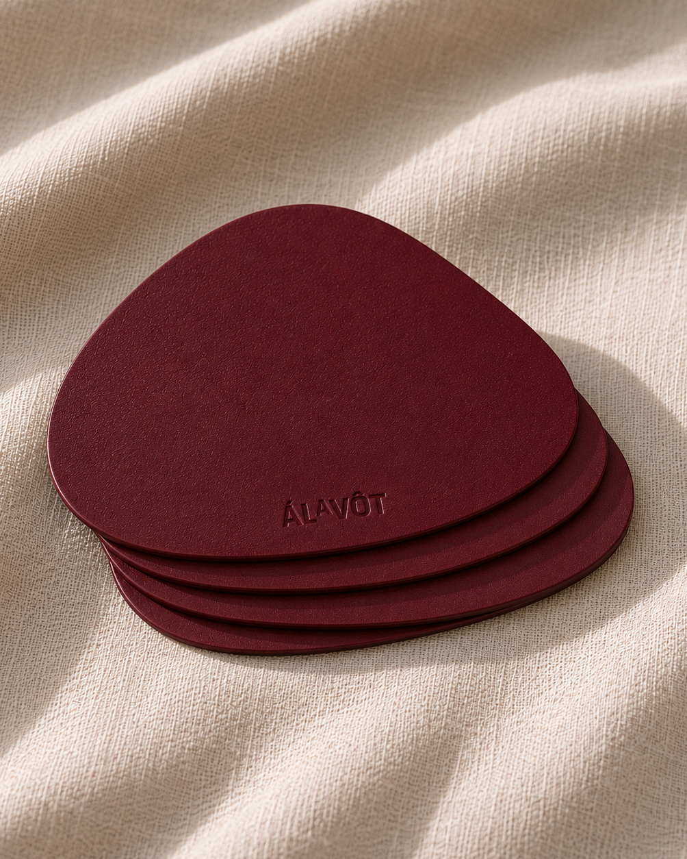 Set of burgandy coasters with 'ALAVOT' branding on a beige fabric background