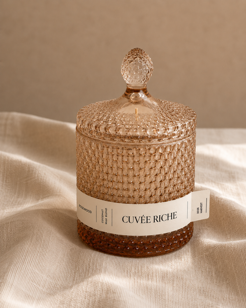 Cuvée Riche scented candle with textured glass lid on beige fabric