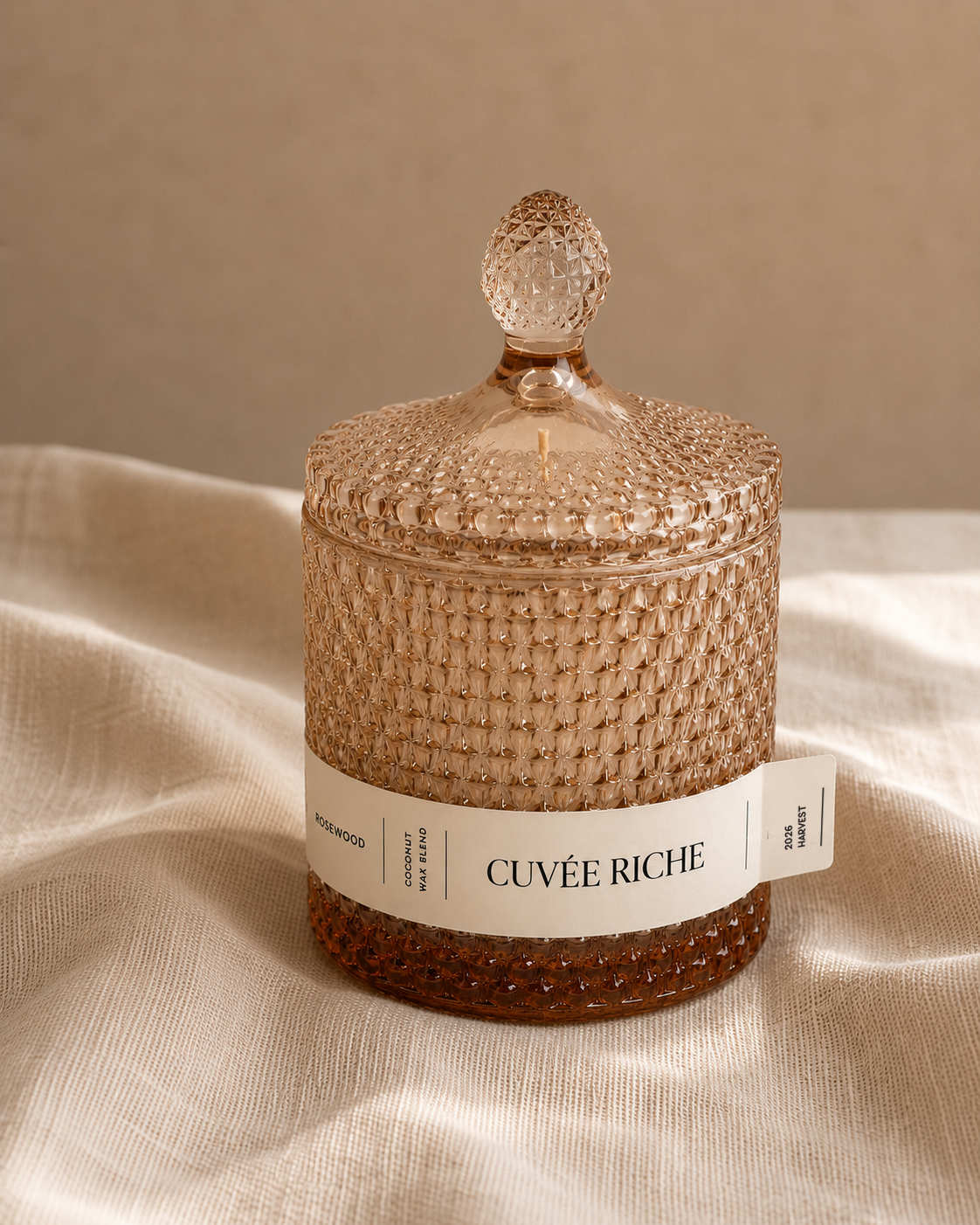 Cuvée Riche scented candle with textured glass lid on beige fabric