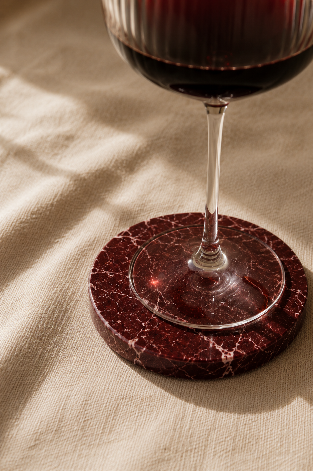 Wine glass on a red marble coaster with a beige fabric background