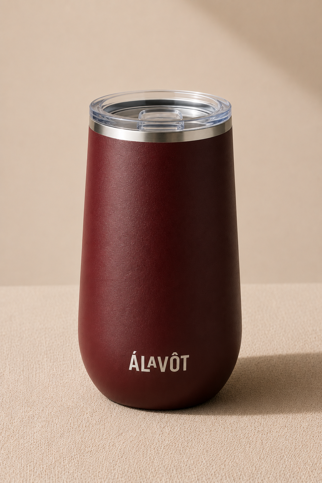 Maroon wine tumbler with silver lid on a beige background