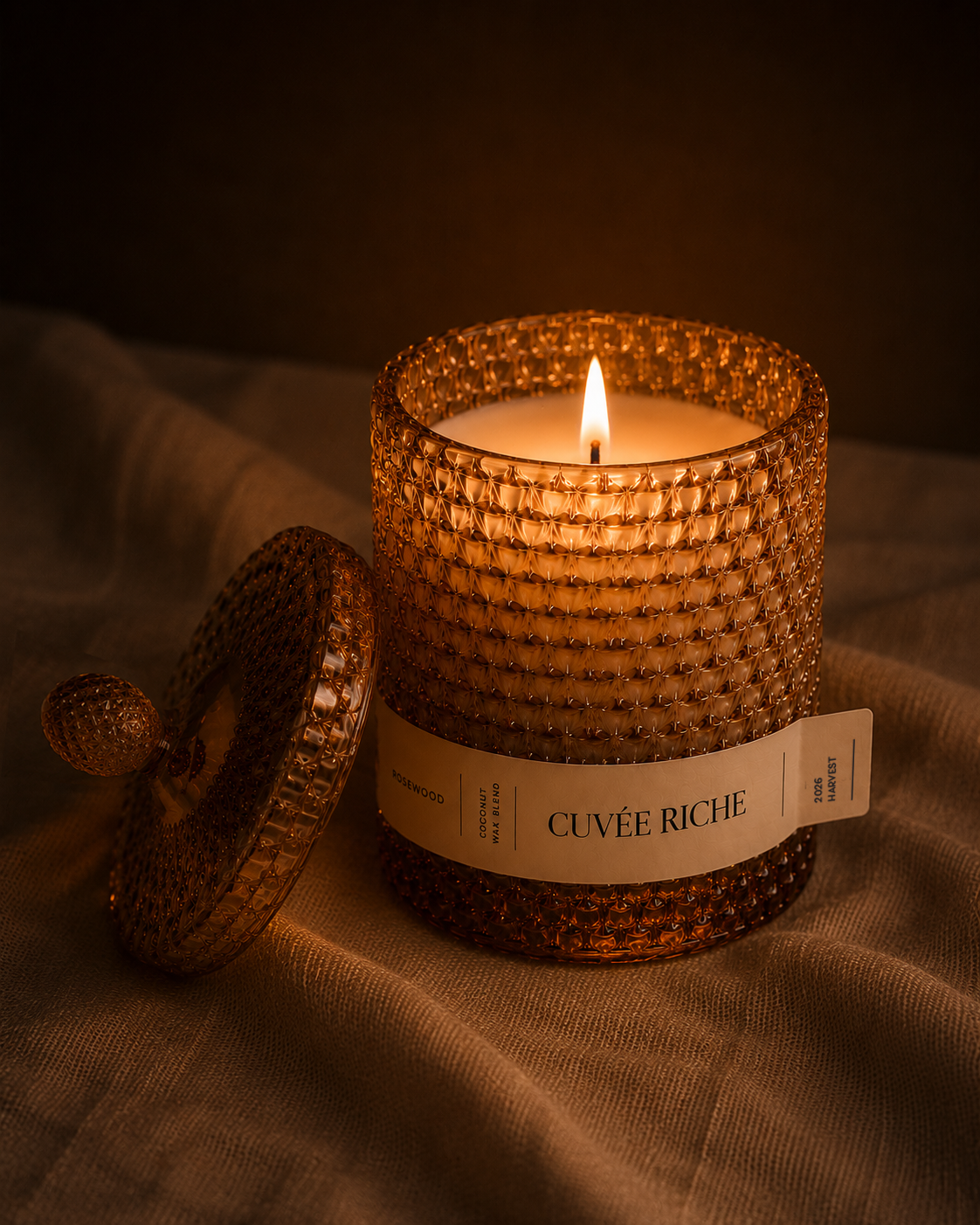 Scented candle with a champagne coloured textured glass holder labeled 'Cuveé Riche' on a textured surface.