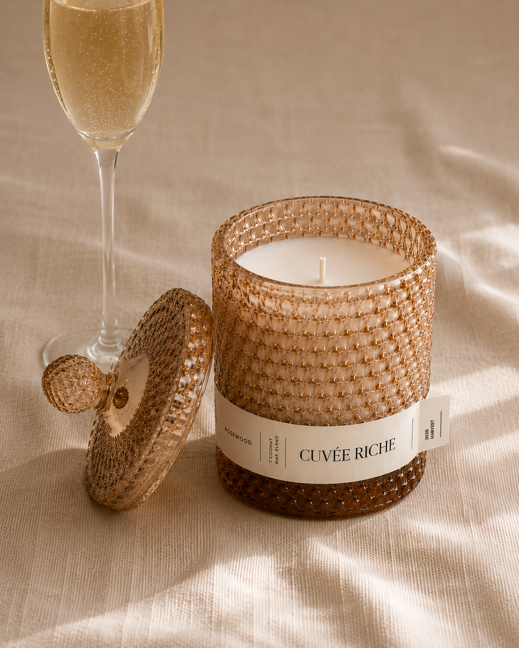 Scented candle labeled 'Cuveé Riche' next to a glass of champagne on a textured surface