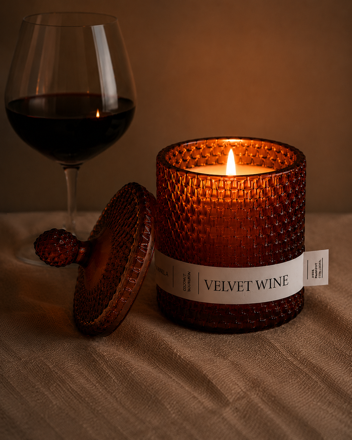 Candle labeled 'Velvet Wine' next to a glass of red wine on a textured surface.